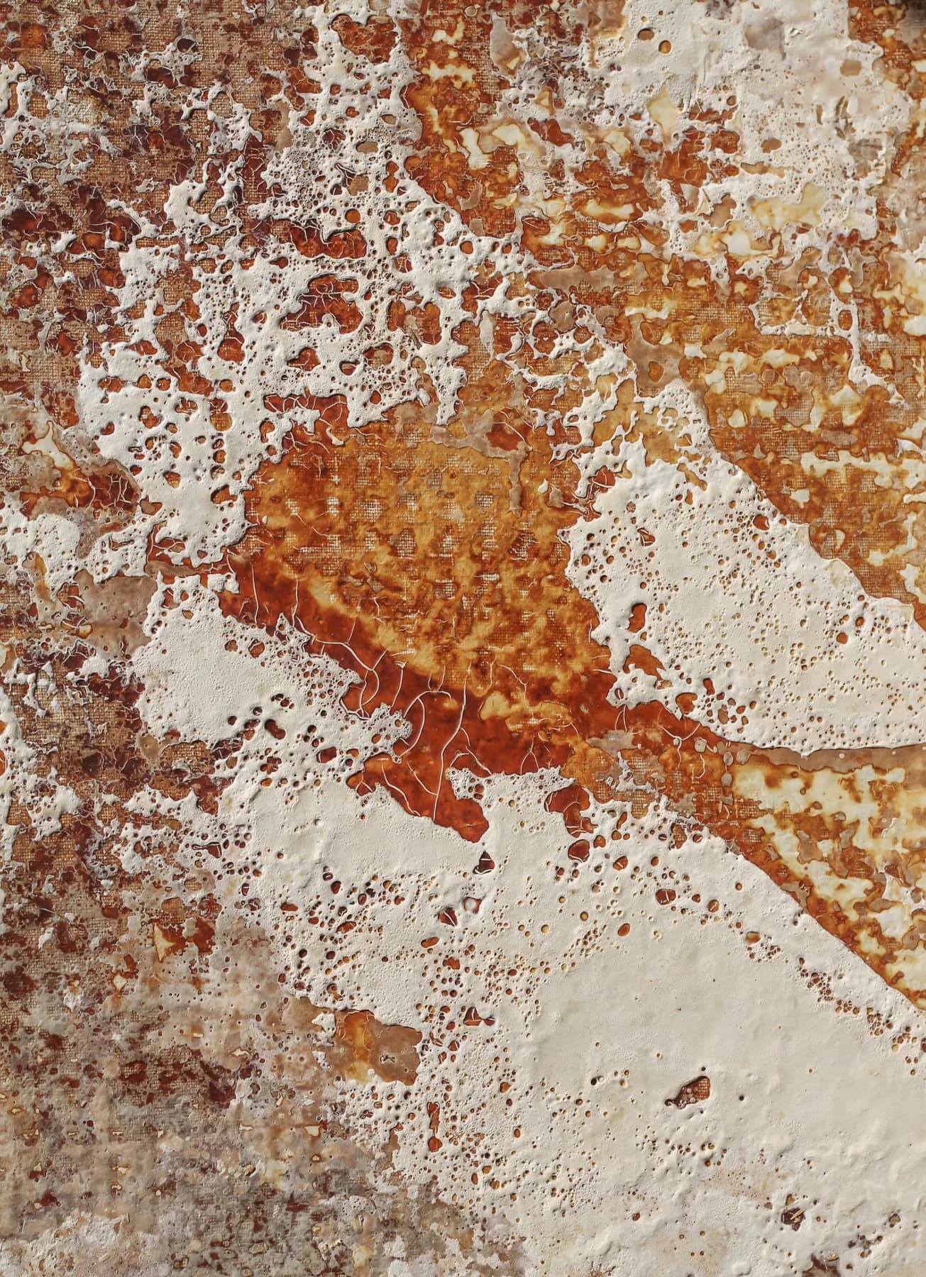 Close-up of a cream surface flecked and pooled with bright orange and rust.