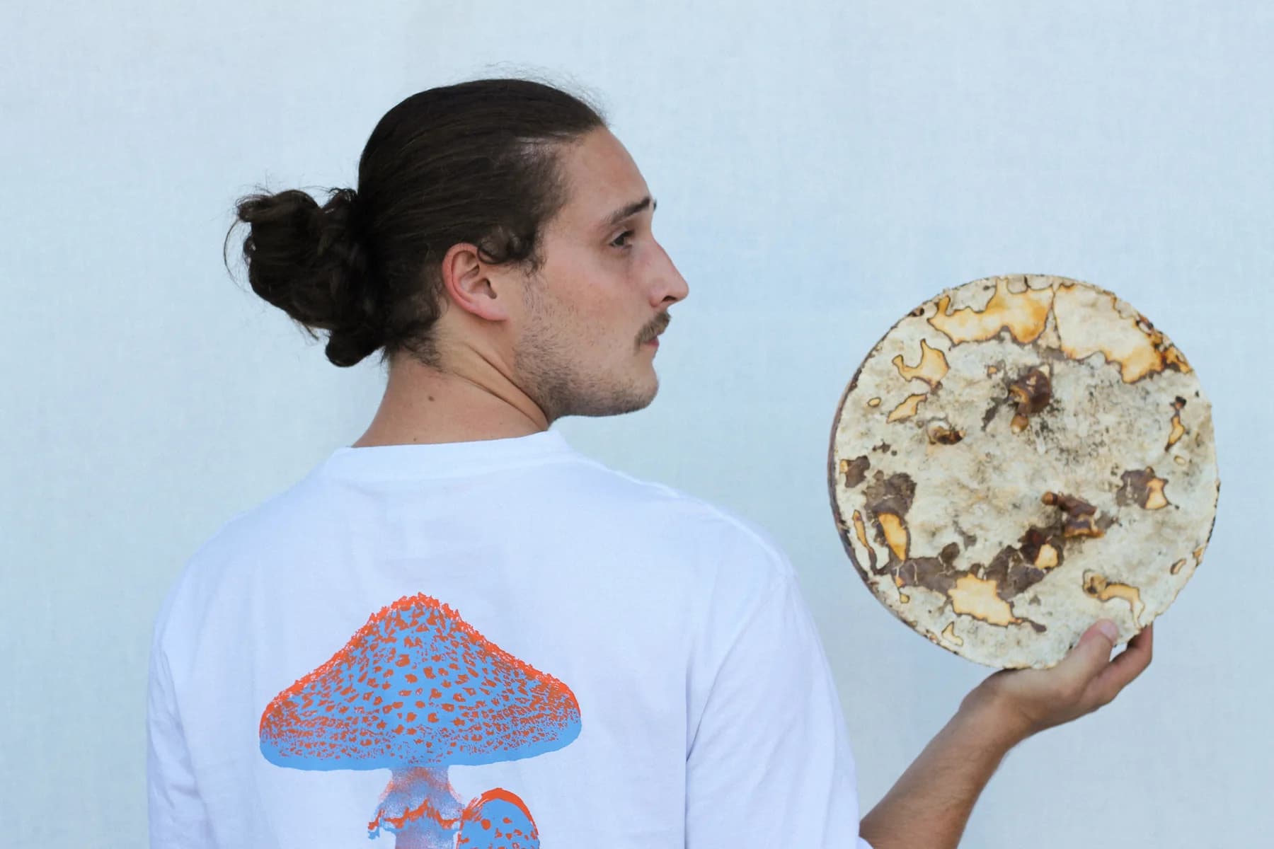 Andy Cartier in profile, holding a circular panel with cream, rust and ochre textures.