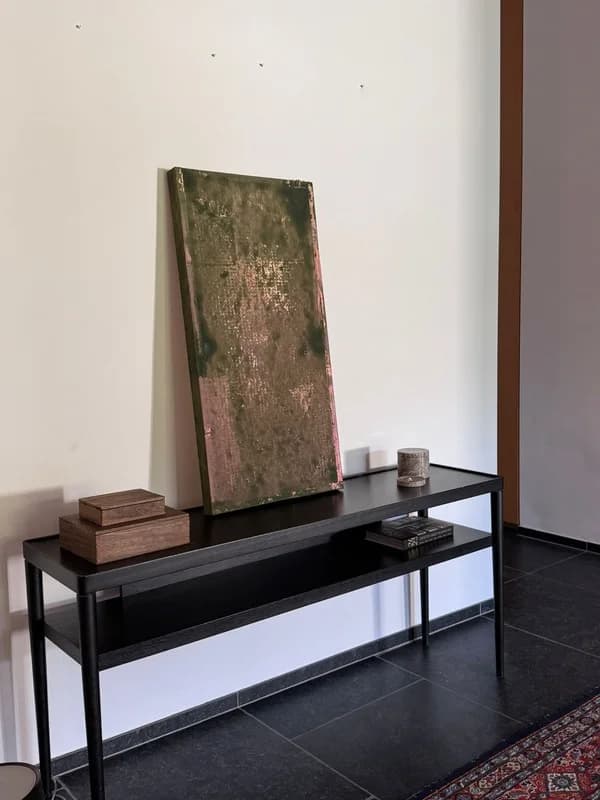 A green and pink textured panel leaning on a black console table in a hallway.