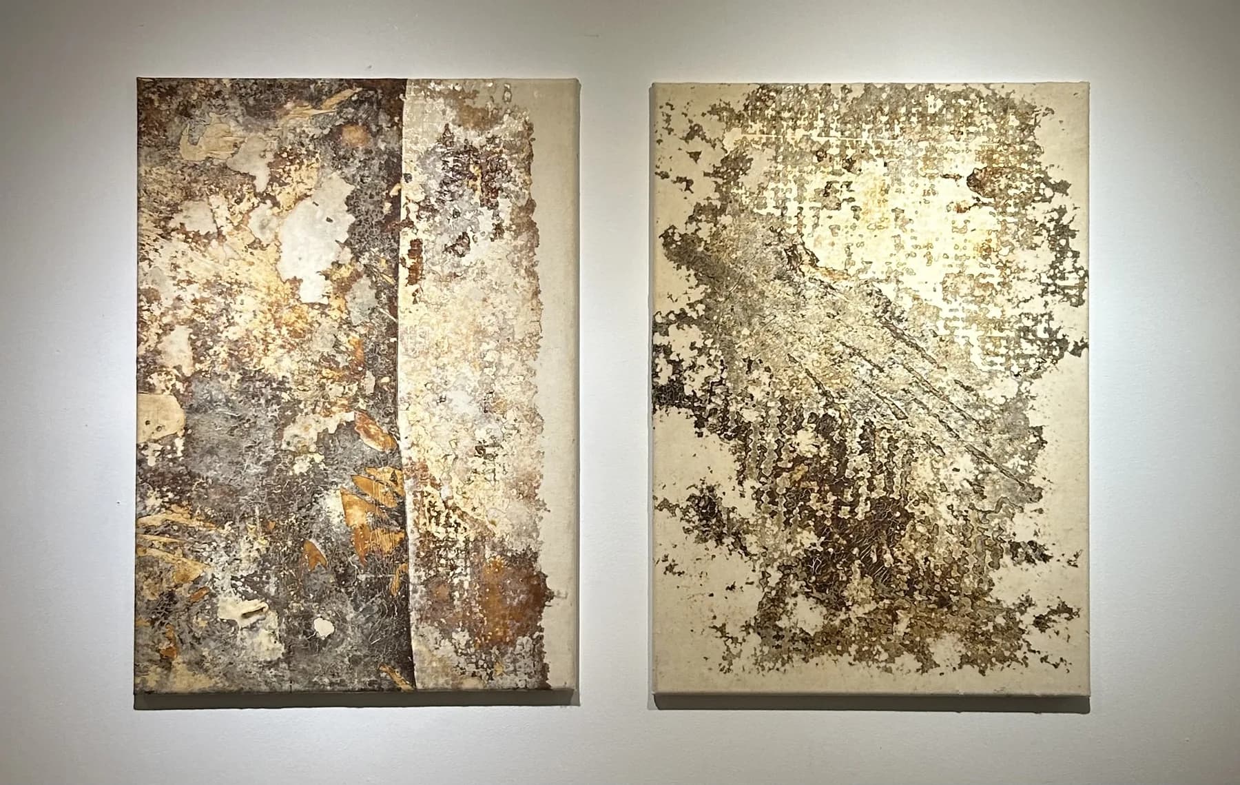 Two vertical panels with gold, bronze and cream textures, lit on a white gallery wall.