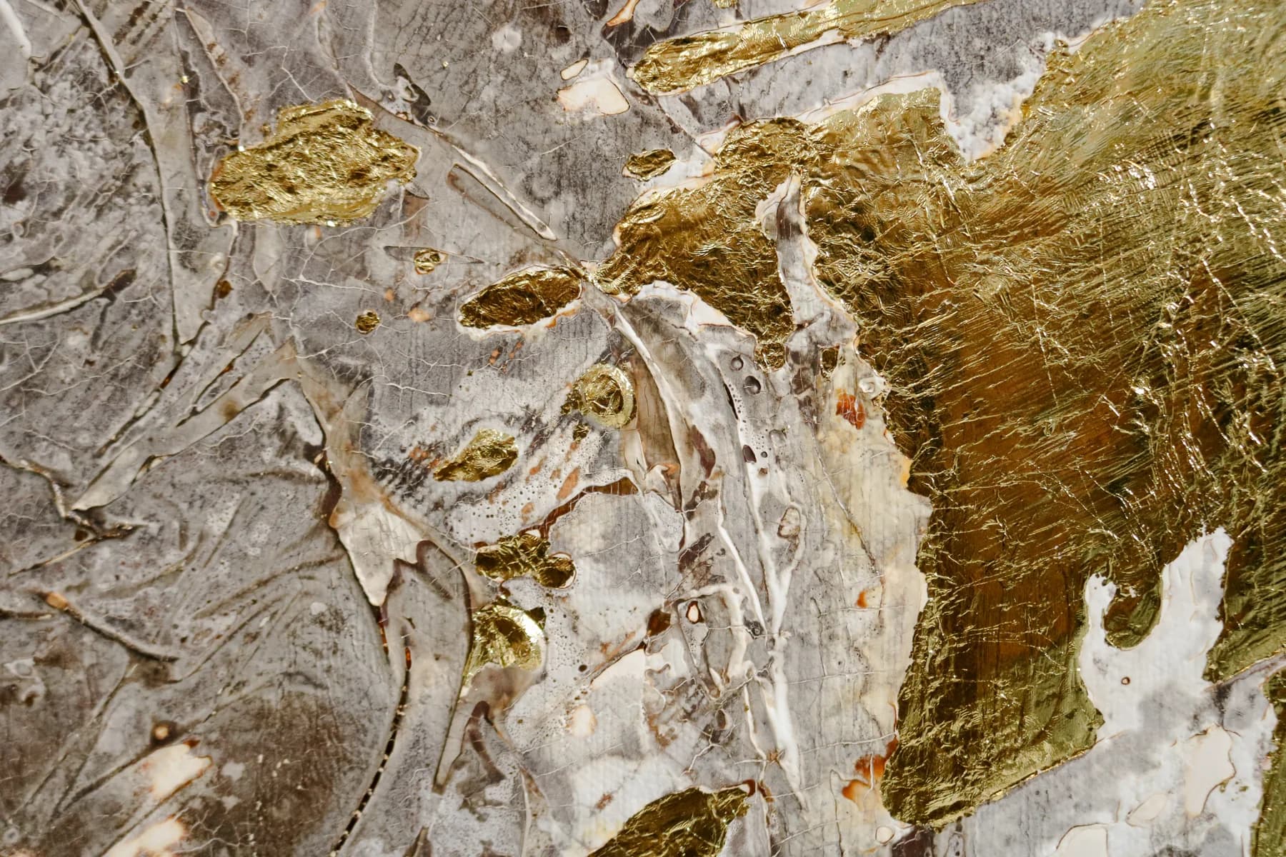 Close-up of gold leaf laid over a silver-grey surface full of folds and ridges.