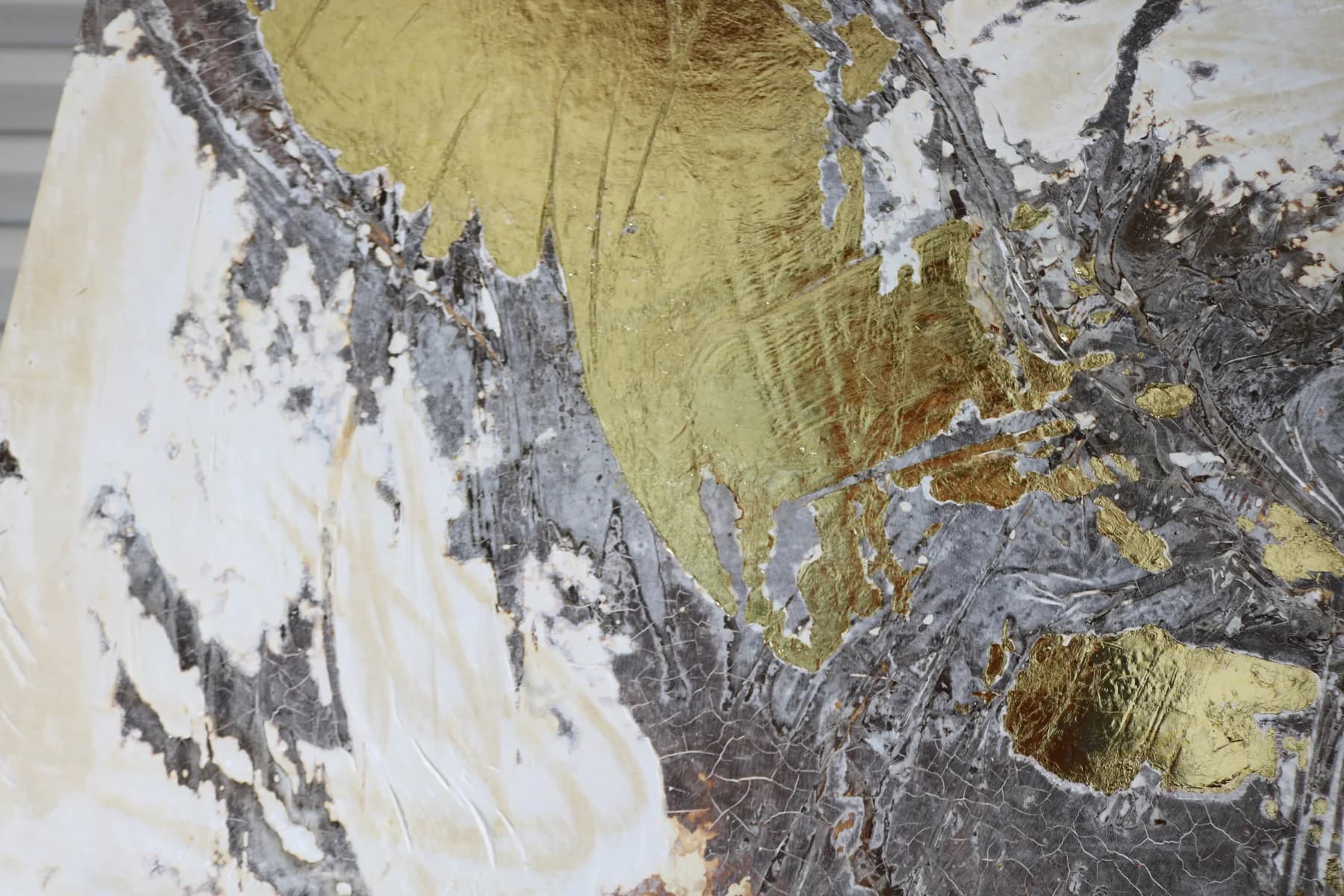 Close-up where gold leaf meets a folded silver-grey surface and white ground.
