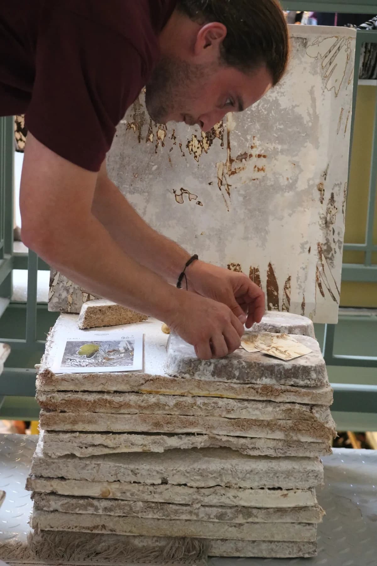 Andy Cartier arranging small grown pieces on a stack of panels, with a large work behind.