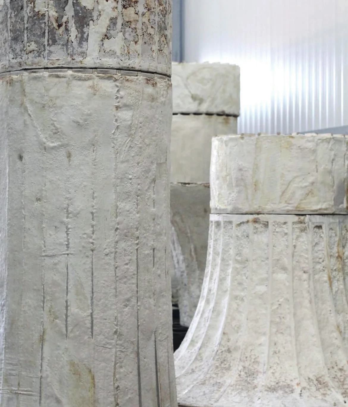 Tall cream-coloured grown columns with vertical lines and a flared top, standing indoors.