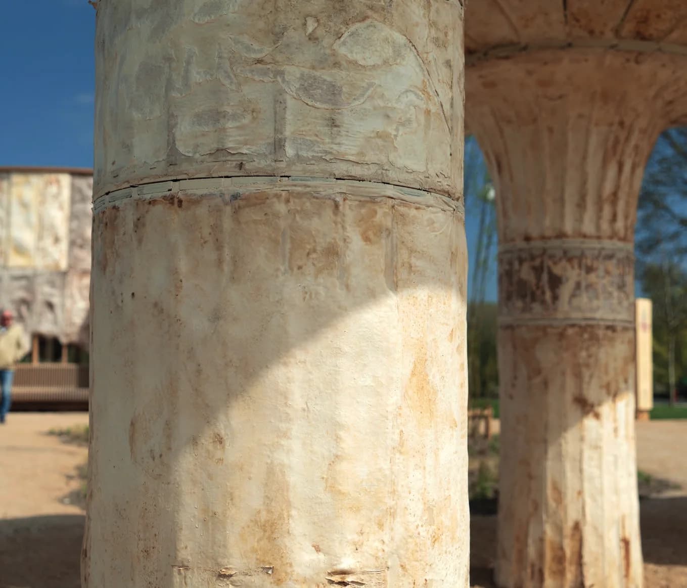 Close view of two grown columns outdoors, with weathered cream and rust tones and a band where the column meets the cap.