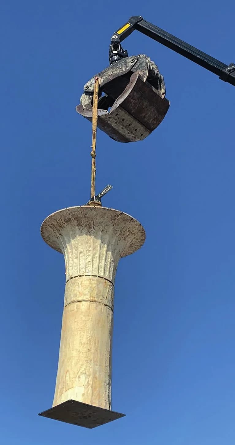 A grown column hanging from a crane grab against a clear blue sky.